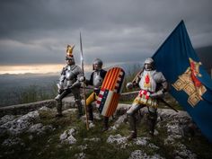 three knights holding flags on top of a hill