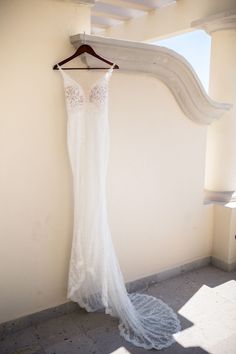 a wedding dress hanging up on a hanger in front of a white stucco wall