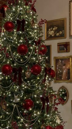 a christmas tree with red and white ornaments on it in front of some framed pictures