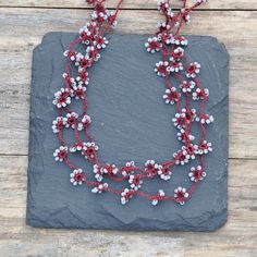 a red and white beaded necklace sitting on top of a slate slab with beads