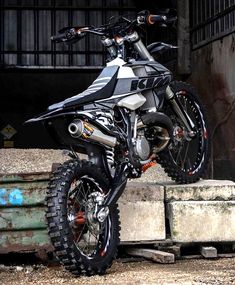 a black and white dirt bike parked in front of a metal structure with graffiti on it