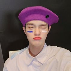 a young man wearing a purple beret with blue stripes on his forehead and nose