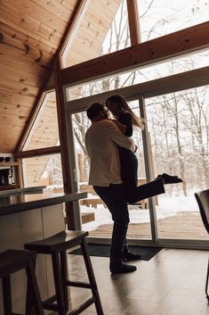 a man and woman hug in front of a glass door as they stand on the kitchen floor