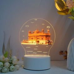 a light up snow globe with an image of a building in the middle and flowers around it