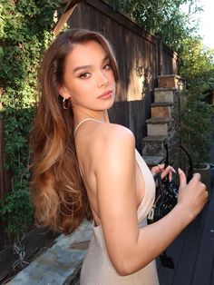 a beautiful young woman standing next to a wooden fence