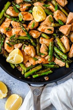 chicken and asparagus stir fry in a skillet with lemon slices on the side