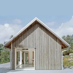 a wooden house sitting on top of a cement floor next to a lush green field