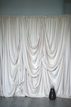 a vase sitting in front of a curtained wall with white drapes on it