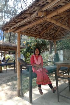 a woman sitting on top of a bench under a wooden roof