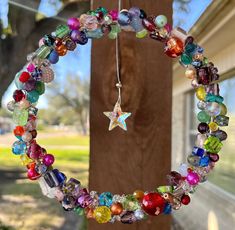 a colorful beaded wreath hanging from a wooden pole next to a tree in front of a house