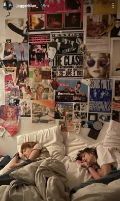 two children sleeping on a bed in front of a wall with pictures and posters all over it