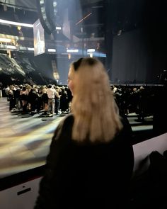 a woman standing in front of a large screen at a convention or show with lots of people