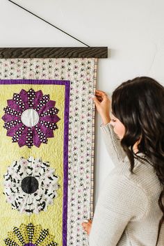 a woman working on a wall hanging quilt