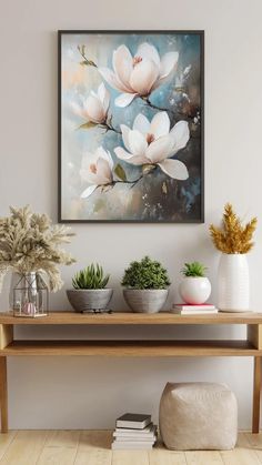 a painting hanging on the wall above a wooden table with potted plants and books