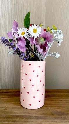 a pink vase filled with lots of flowers on top of a wooden table