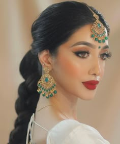 a woman with long black hair wearing green and gold jewelry on her head, looking off to the side