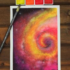 an art project with paint and watercolors on the table next to it is a drawing of a spiral galaxy