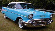 an old blue and white car is parked in the grass