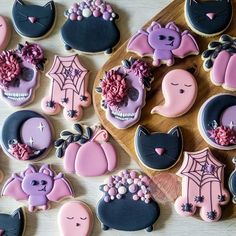 many decorated cookies are on a wooden board with pink and black icing, along with other decorations