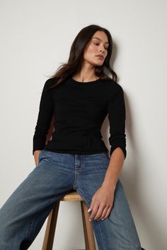 A person with long dark hair sits on a wooden stool Fitted Long Sleeve T-shirt For Everyday, Minimalist Black Top For Fall, Minimalist Long Sleeve Top For Everyday, Fitted Long Sleeve Top With Crew Neck, Basic Fitted Long Sleeve Top For Everyday, Velvet Tees, Fitted Long Sleeve, 12th Grade, We Made It