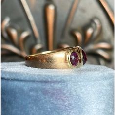 Imagine the opulence of a Victorian evening—gaslights flickering in the London mist, and beneath it all, a flash of deep red catches the light. This ring is a rare beauty from that era, a true testament to the elegance of its time. The three almondine garnets—smooth, cabochon-cut—glow with a soft, mysterious warmth, each stone embodying the passion and refinement of the period. Thick, buttery 18 karat gold wraps them in a band that speaks not just of wealth, but of a quiet, timeless grace.  At its front, the ring measures 8.3 mm north to south and 18.6 mm across, standing 4.6 mm off the finger with a band that narrows to 3.8 mm at the back. The center garnet is a substantial 6.5x5.5x2.6 mm, flanked by two smaller stones, each about 5x4.4x2.2 mm. Fully hallmarked with the crown for England, Luxury Three Stone Ruby Ring, Luxury Oval Three-stone Ruby Ring, Red Domed Anniversary Ring, Red Domed Rings For Anniversary, Formal Red Domed Rings, Luxury Gold Three-stone Ruby Ring, Luxury Gold Ruby Three Stone Ring, Luxury Gold Three Stone Ruby Ring, Luxury Gold Ruby Ring With Three Stones