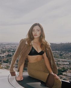 a woman sitting on top of a roof with her legs crossed and looking at the camera