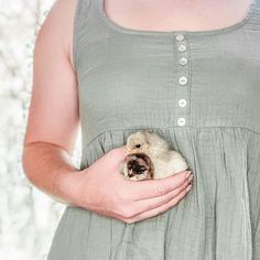 a pregnant woman holding a small animal in her belly while wearing a dress with buttons on it