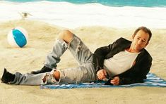 a man laying on top of a beach next to a blue and white ball