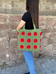 a woman carrying a green crocheted bag with red circles on the front and sides