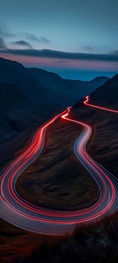 a winding road in the mountains with red light streaks going down it's sides