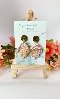 a pair of pink and gold leaf earrings sitting on top of a easel