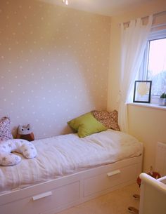 a small white bed sitting under a window next to a wall mounted clock and stuffed animals