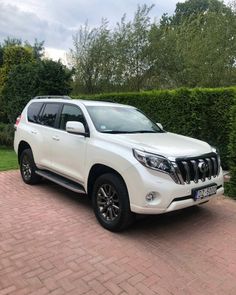 a white toyota land cruiser is parked in front of a hedge and shrubbery on a brick driveway