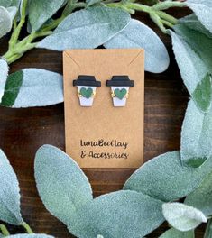 a pair of green and white earrings sitting on top of a wooden table next to leaves