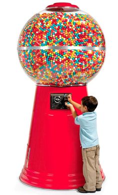 a young boy standing next to a red gummy machine filled with lots of sprinkles