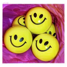 four yellow balls with faces drawn on them sitting in a pink wrapper filled with tissue paper