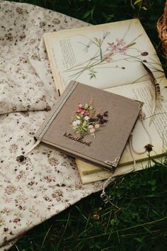 an open book sitting on top of a blanket next to a basket filled with flowers