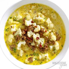 a white bowl filled with soup topped with cauliflower and meatballs, garnished with parsley