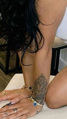 a woman with tattoos on her arm and leg sitting on a bed holding a cell phone