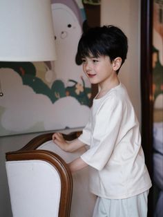 a young boy standing next to a wooden chair