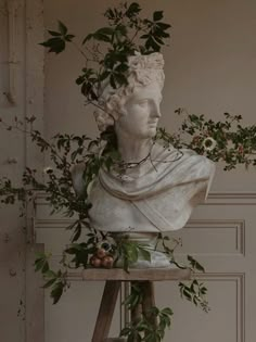 a white statue sitting on top of a wooden table next to a plant filled wall