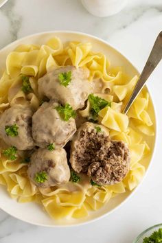 a white bowl filled with meatballs and noodles on top of a marble countertop