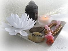 a white flower sitting on top of a tray filled with stones and beads next to a candle