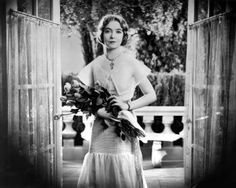 a woman standing in front of an open door holding flowers