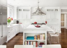 a kitchen with white cabinets and lots of books on the counter top in front of an island