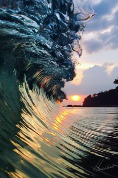 an ocean wave with the sun setting in the background