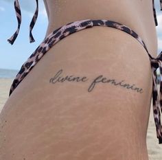 a close up of a person with a tattoo on her stomach and the words divine feminine written in cursive writing