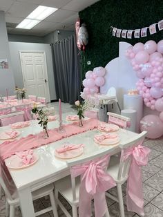 a table set up for a baby shower with pink and white decorations on the wall