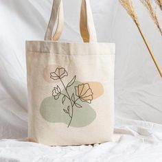 a tote bag sitting on top of a bed next to some dried grass and a plant