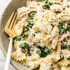 pasta with chicken, spinach and cheese in a white bowl next to a fork